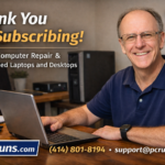 John from PCRuns computer repair smiling at desk helping with laptop and offering honest repair and refurbished computers